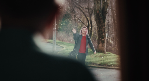Person waves through a doorway, viewed from behind another's silhouette.