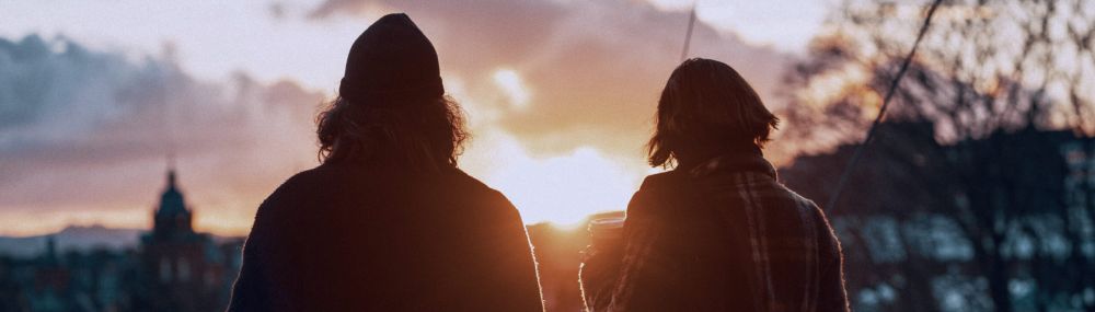 Two people watching sunset in city, silhouetted against a vibrant sky.