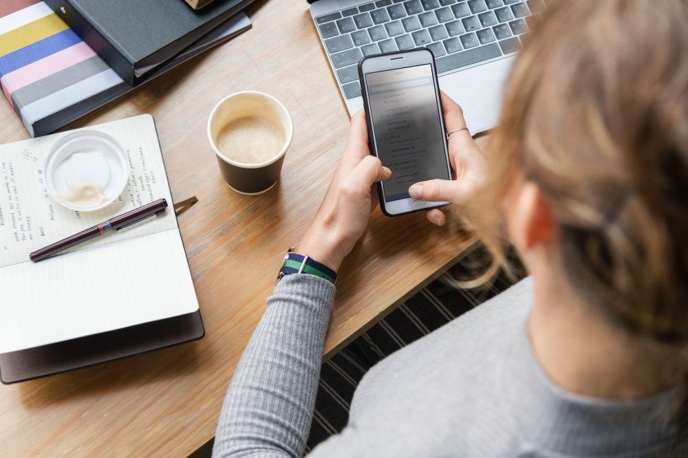 Woman on phone sitting at a desk with coffee and a laptop next to her.