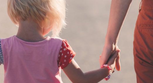 Child in a pink shirt holding hands with an adult, focus on joined hands, warm tones.