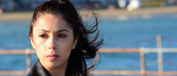 Person with windswept hair by a waterfront with a railing.