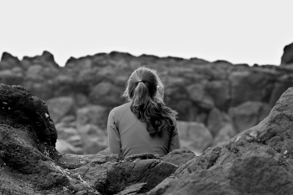 Person sitting facing away on rocky terrain in black and white.