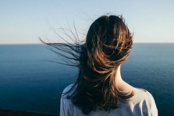 Woman with hair blowing in the wind, gazing at a serene sea.