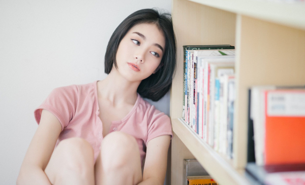 Person in pink top sitting by a bookshelf.