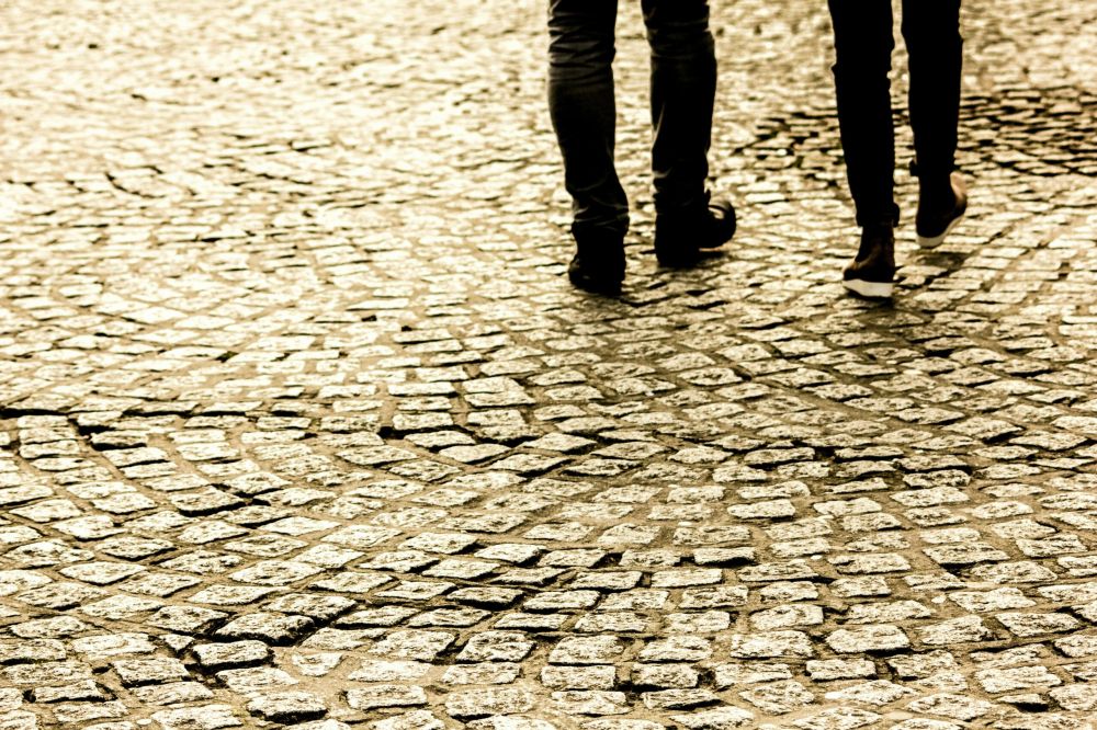 Two people walking on a cobblestone street, shown from the knees down.