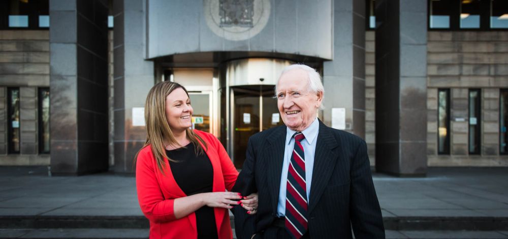 Two professionals in business attire standing in front of an office building entrance.