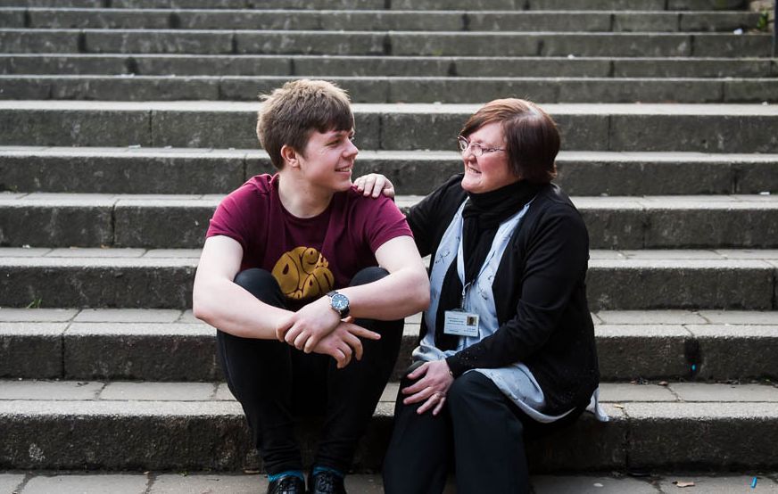 A man and woman sitting on outside steps, the woman is comforting the man.
