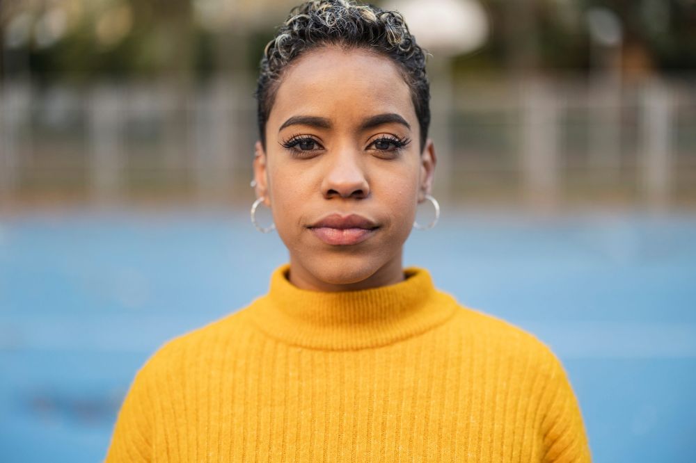 A young woman with hoop earrings and a yellow turtleneck.