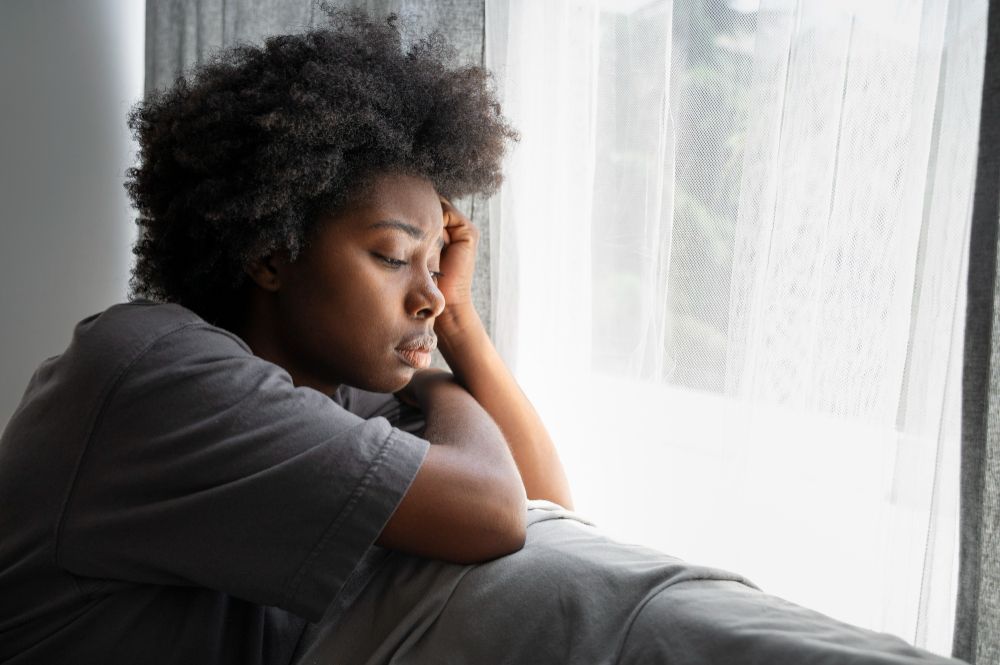 Person sitting by the window resting their head on their hands.